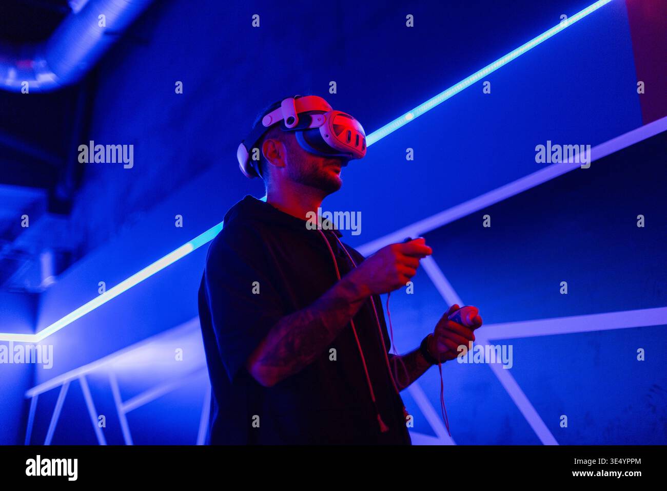 Fashion-Tech-Mann mit VR-Headset-Brille mit Joysticks, Spiel in dunklen Räumen mit Neonlicht Stockfoto