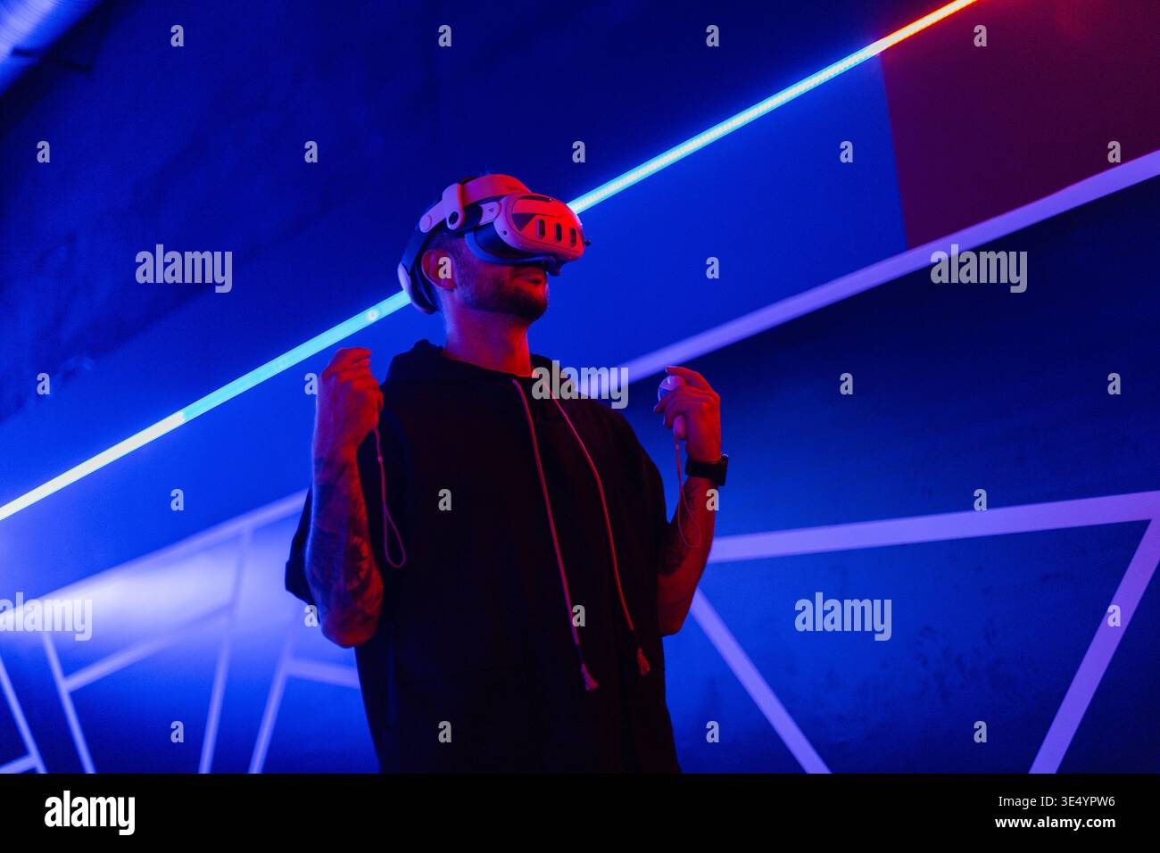 Cooler trendiger Mann in vr-Brille, der 360°-Videos mit Virtual-Reality-Headset auf dunklem Hintergrund mit Neonlicht ansieht. Der Kerl hält einen Joystick und pla Stockfoto