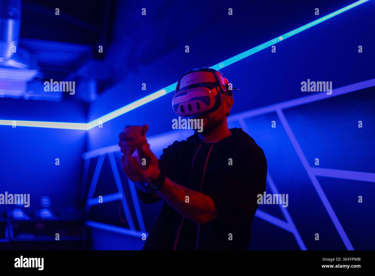 Schöner, stylischer, cooler Gamer-Mann mit VR-Brille, die Joysticks hält und virtuelles Spiel im neonhellen Spielzimmer spielt. Virtual-Reality-Technologie Stockfoto