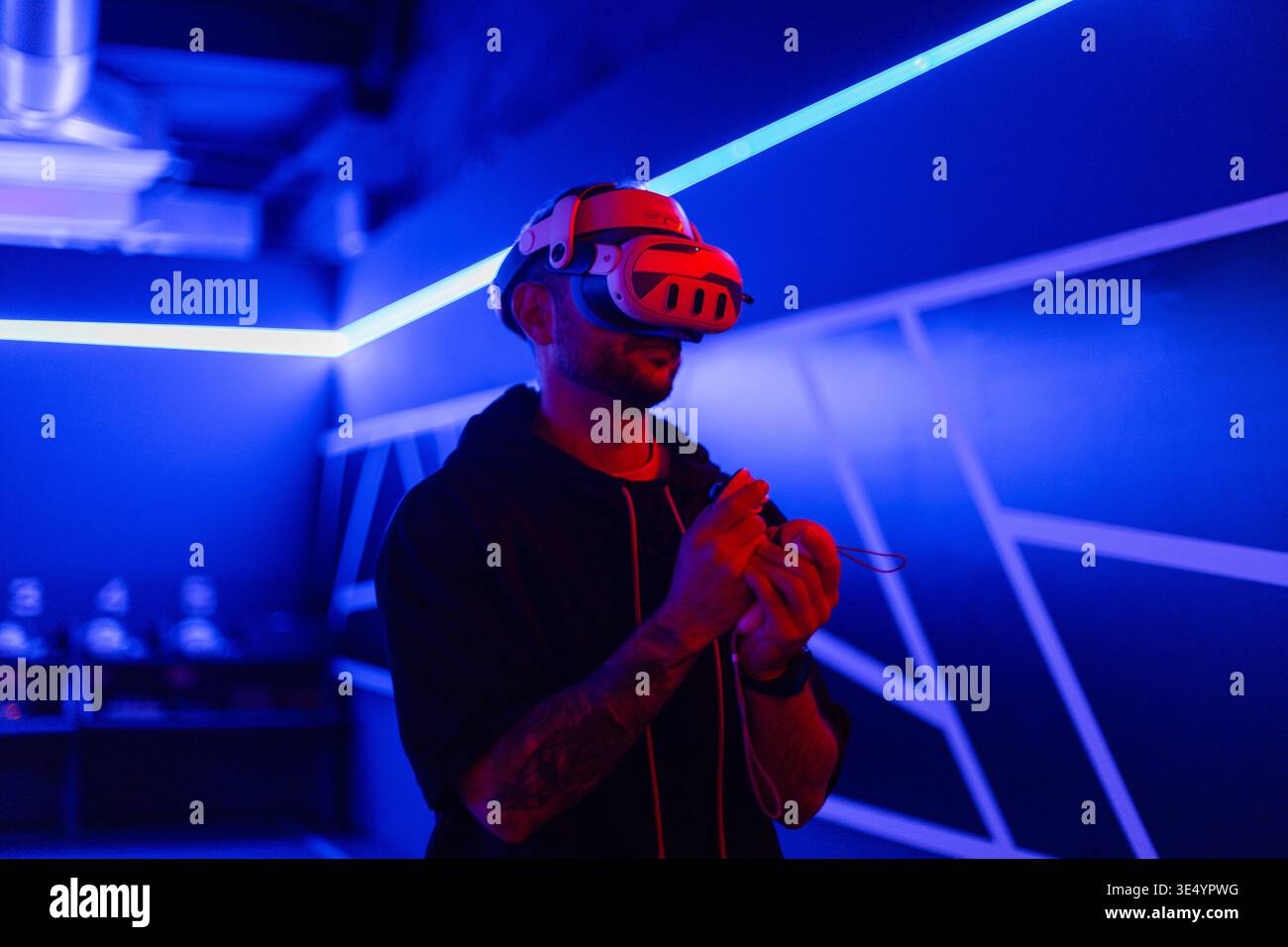 Coole Mode-Mann in VR-Headset-Brille mit Joystick, die Spiele in dunklen Räumen mit Neonlicht spielt Stockfoto