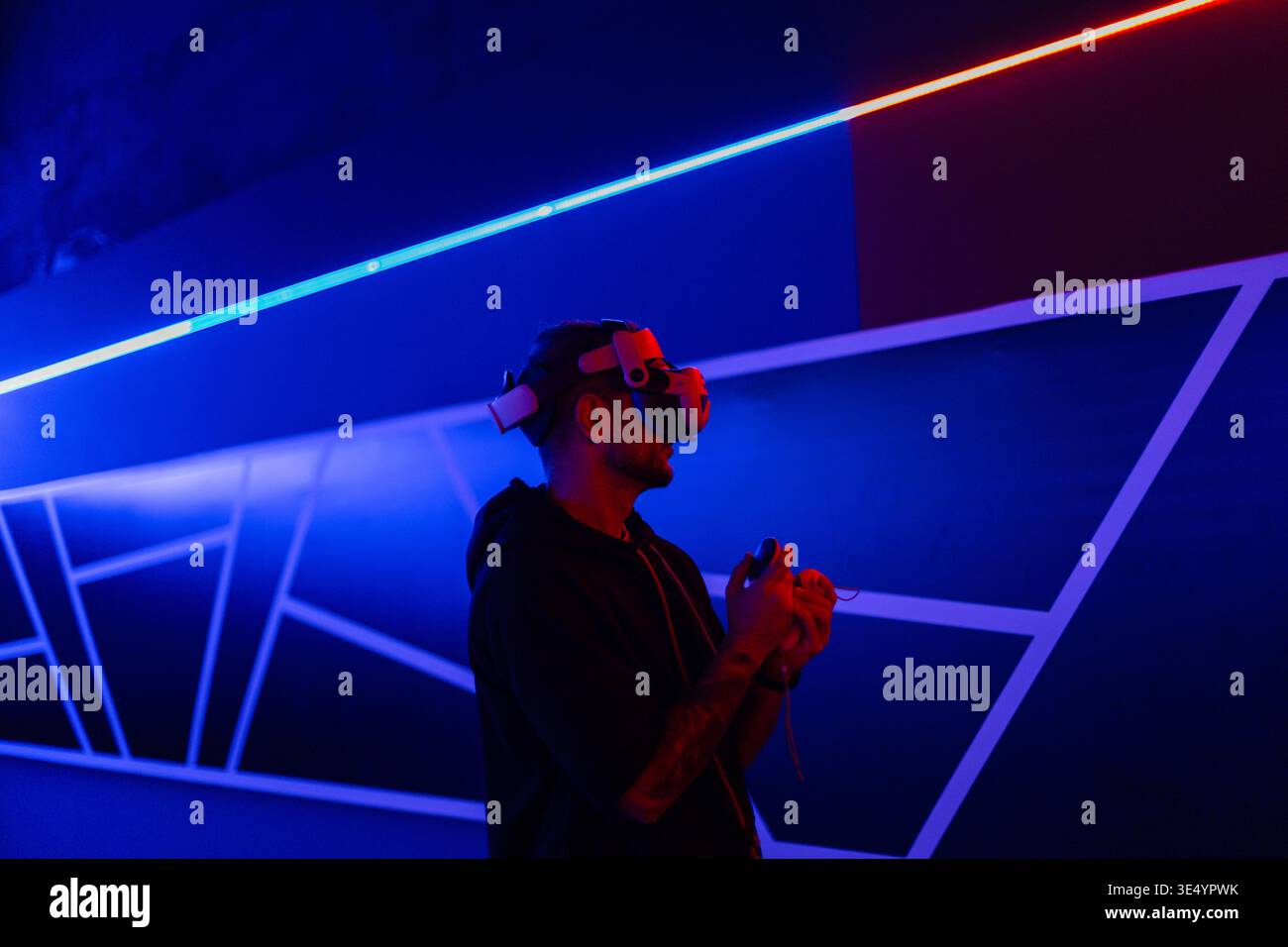 Fashion-Tech-Mann mit VR-Headset-Brille mit Joysticks, Spiel in dunklen Räumen mit Neonlicht Stockfoto