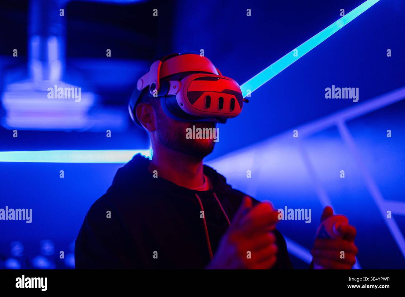 Fashion-Tech-Mann mit VR-Headset-Brille mit Joysticks, Spiel in dunklen Räumen mit Neonlicht Stockfoto