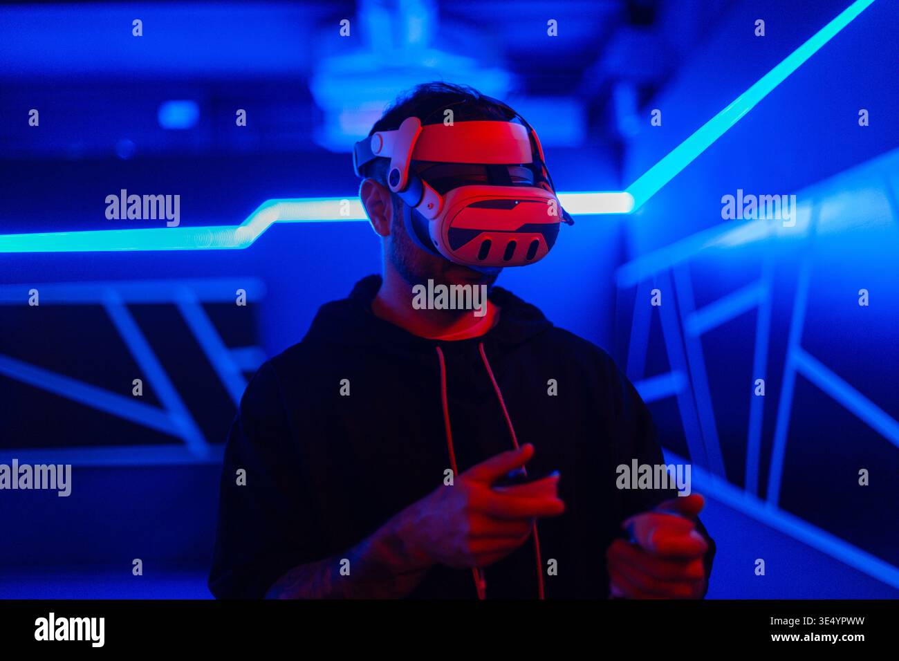 Schöner, stylischer, cooler Gamer-Mann mit VR-Brille, die Joysticks hält und virtuelles Spiel im neonhellen Spielzimmer spielt. Virtual-Reality-Technologie Stockfoto