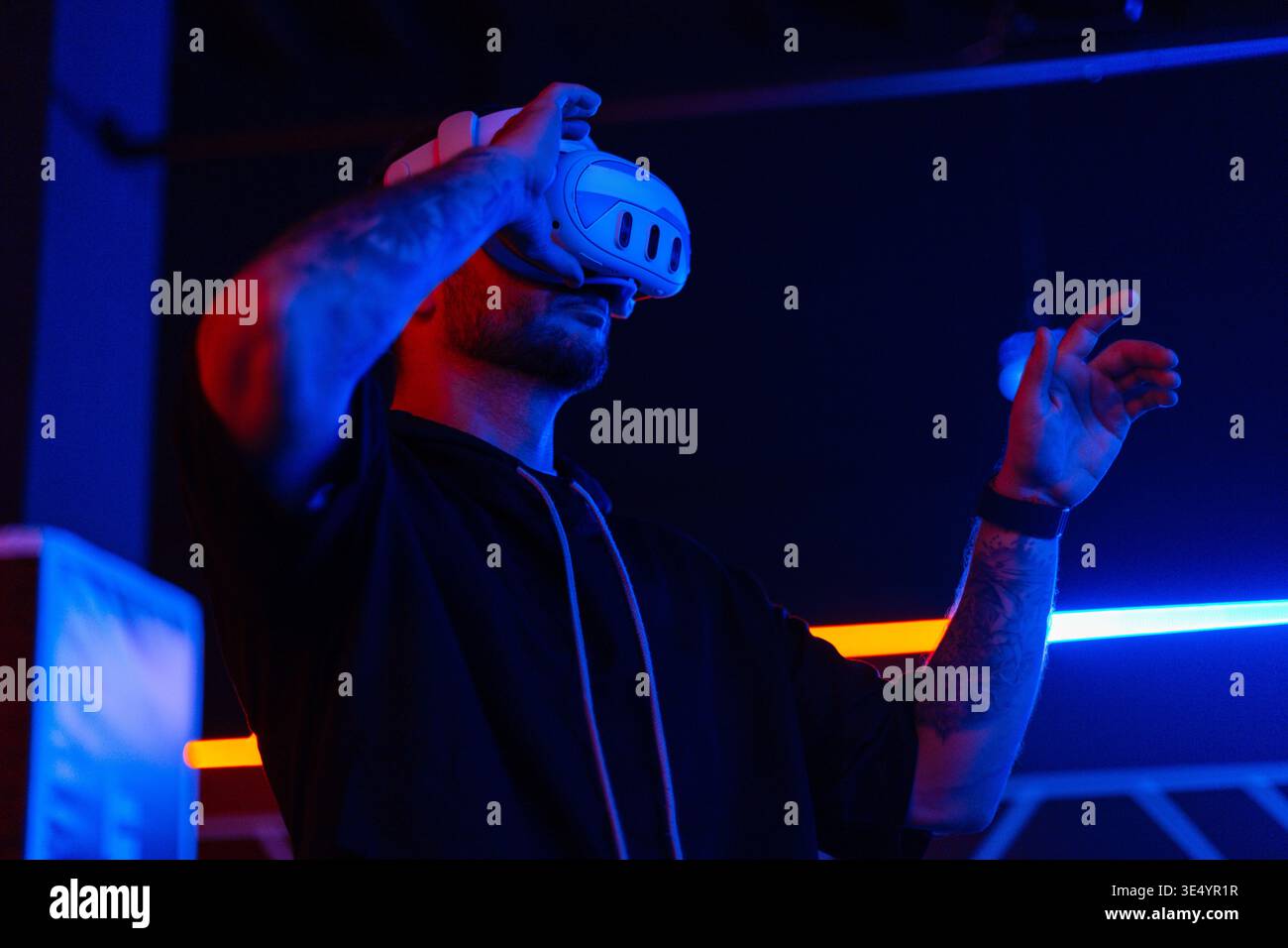 Coole, gutaussehende Modetechniker mit VR-Brille steuern das virtuelle Menü und berühren den Finger im dunklen Raum mit Neonlicht Stockfoto
