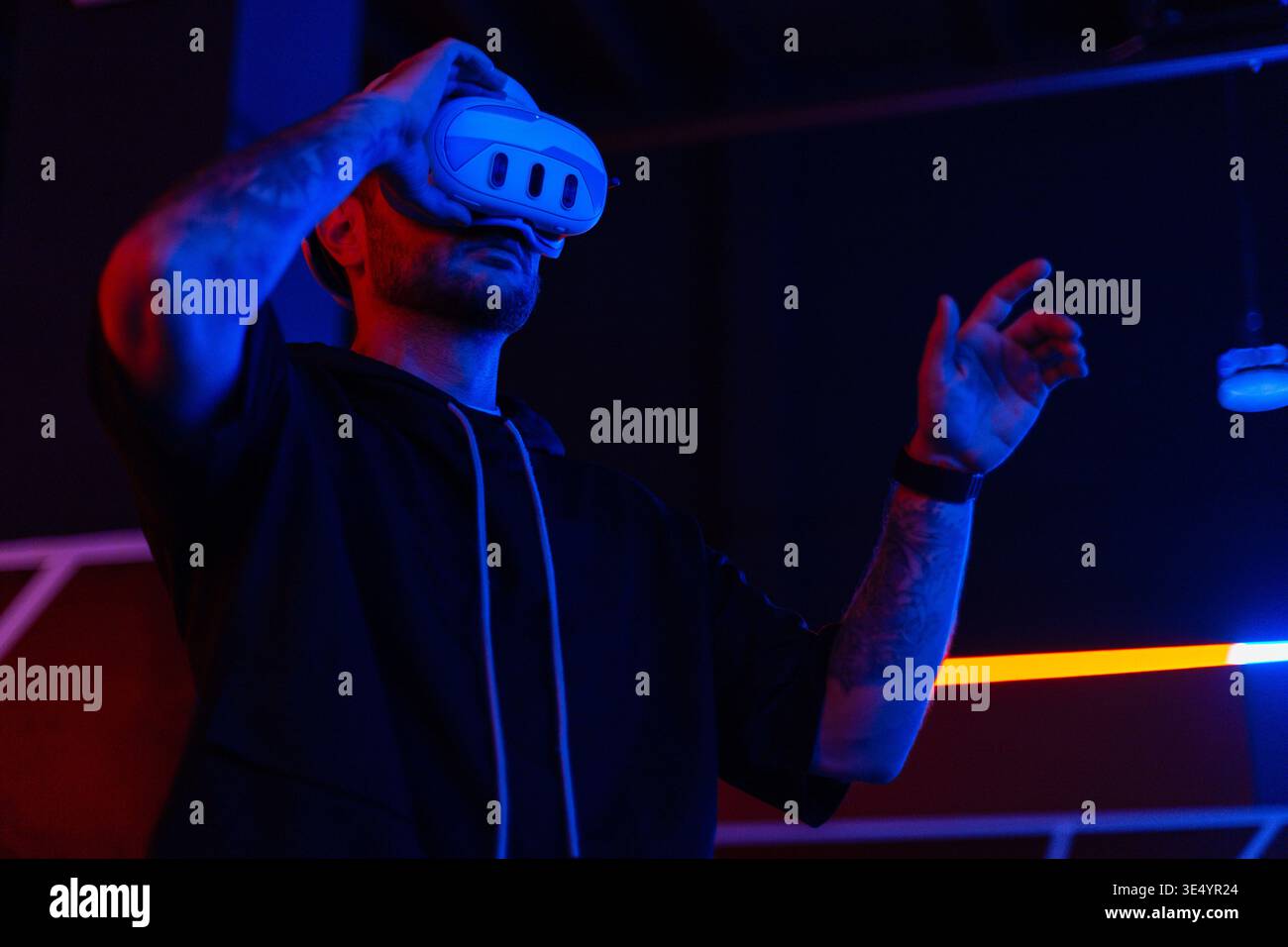 Coole Techniker mit VR-Headset-Brille steuert virtuelles Menü in dunklen Räumen mit Neonlicht Stockfoto