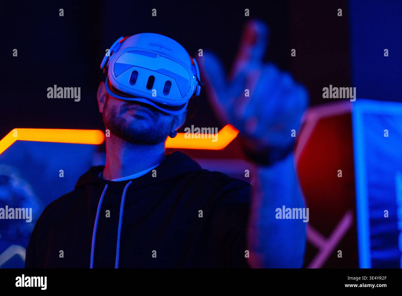 Trendiger Mann in VR-Brille, spielt Videospiele mit Virtual-Reality-Headset, versucht, etwas mit der Hand im Raum mit Neonlicht zu berühren Stockfoto