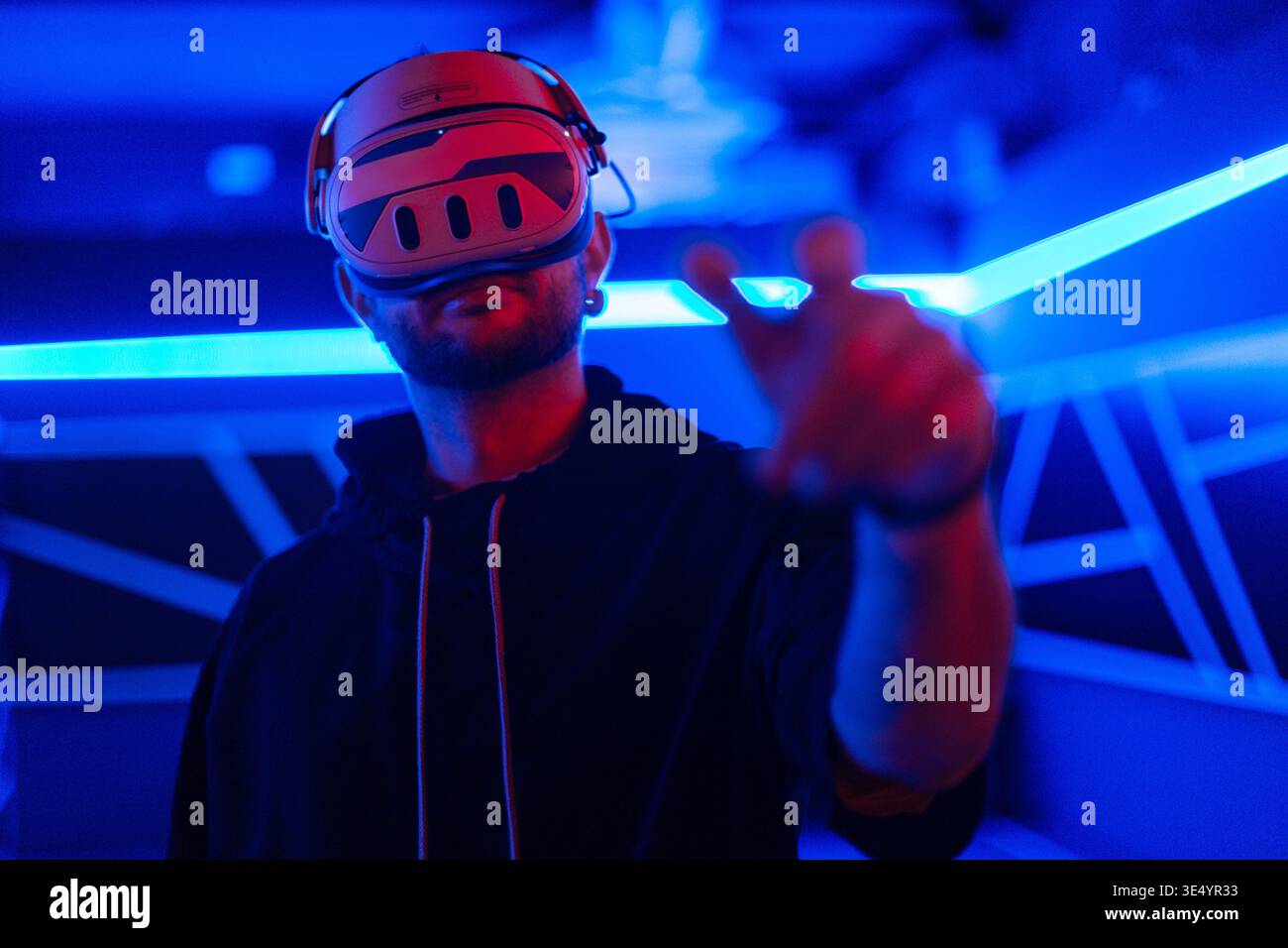 Coole Techniker mit VR-Headset-Brille steuert virtuelles Menü und berührt mit dem Finger in dunklen Räumen mit Neonlicht Stockfoto