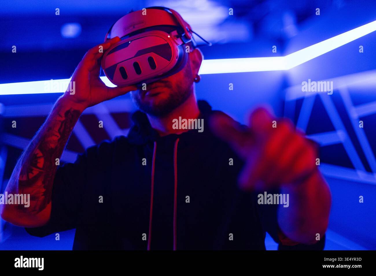 Coole, gutaussehende Modetechniker mit VR-Brille steuern das virtuelle Menü und berühren den Finger im dunklen Raum mit Neonlicht Stockfoto