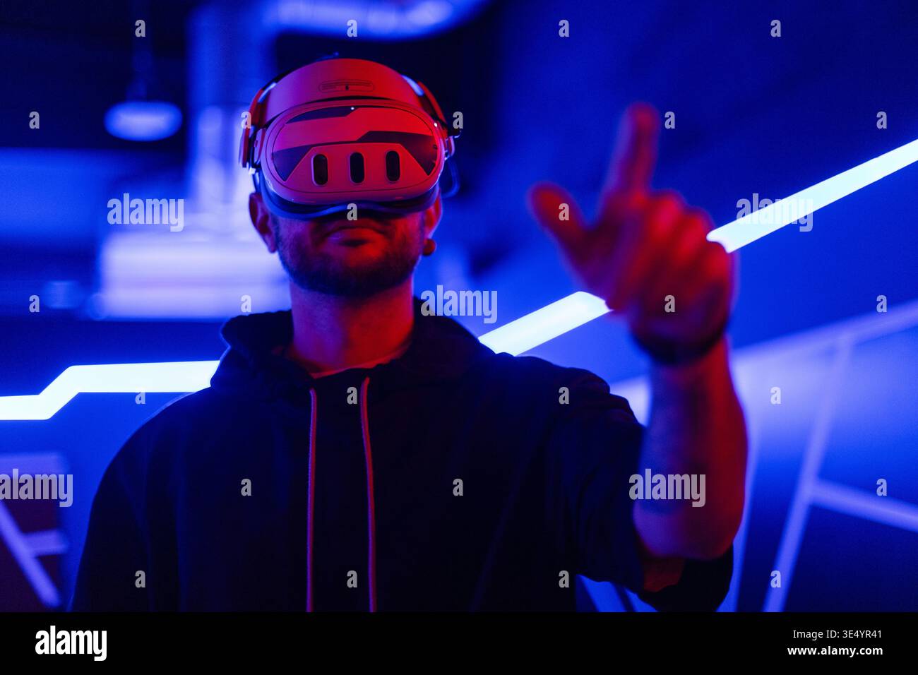 Coole Techniker mit VR-Headset-Brille steuert virtuelles Menü und berührt mit dem Finger in dunklen Räumen mit Neonlicht Stockfoto