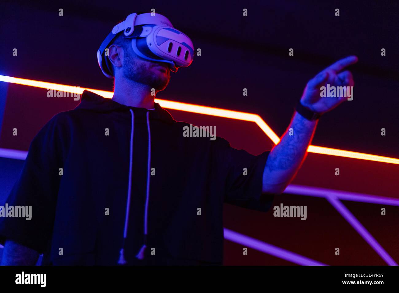 Coole Techniker mit VR-Headset-Brille steuert virtuelles Menü und berührt mit dem Finger in dunklen Räumen mit Neonlicht Stockfoto