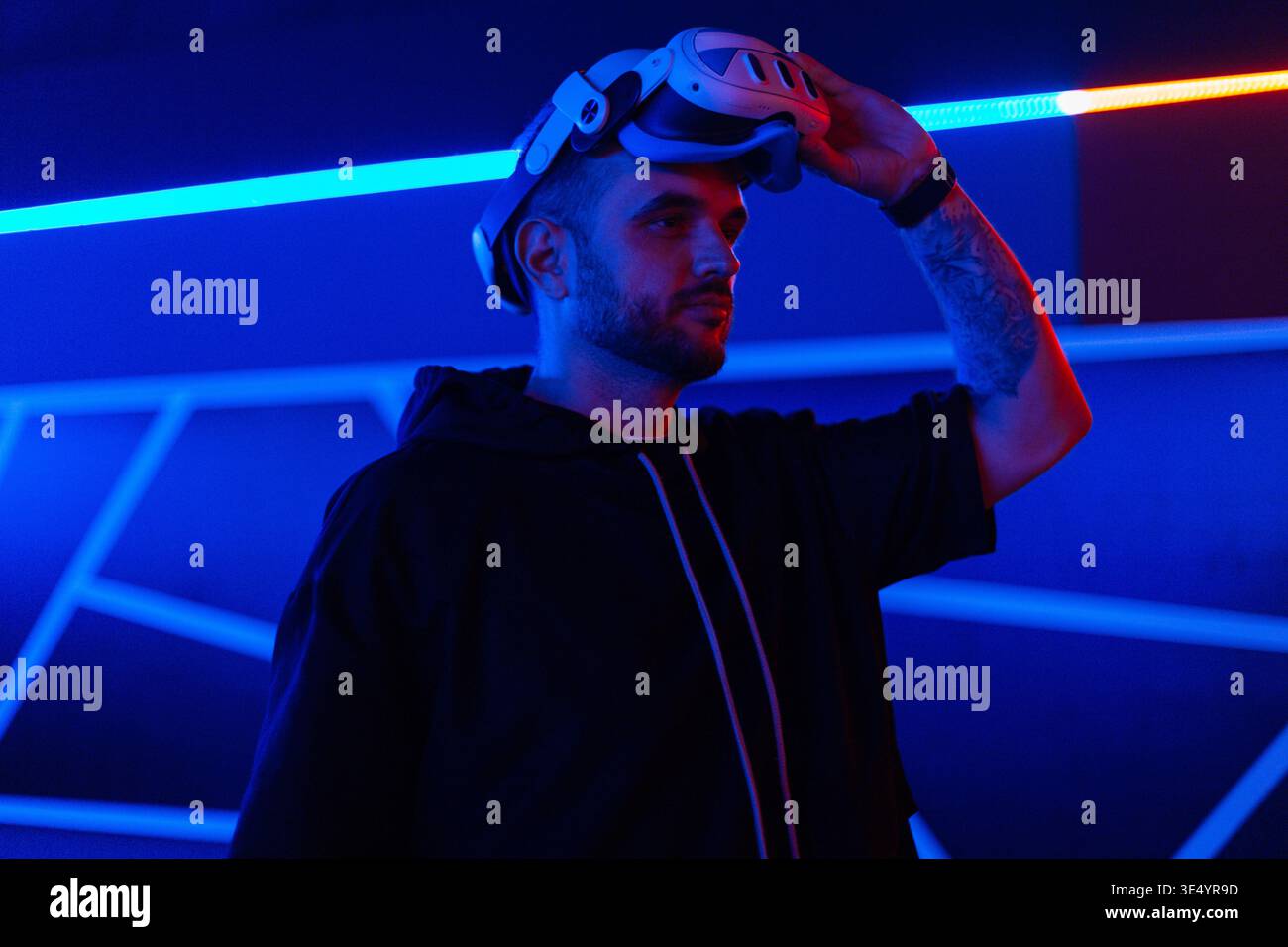 Cooler professioneller Mann, der eine VR-Brille auf dunklem Hintergrund mit Neonblau und rotem Licht aufsetzt. Zukunftstechnologie, Gaming, Unterhaltung und Menschen Stockfoto