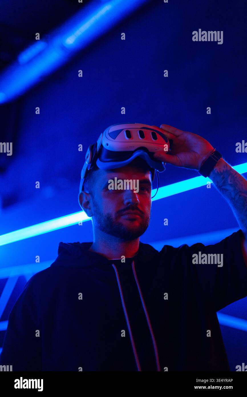 Cooler, gutaussehender Modetechniker, der eine VR-Brille in einem dunklen Raum mit Neonlicht trägt. Virtuelle Realität Stockfoto