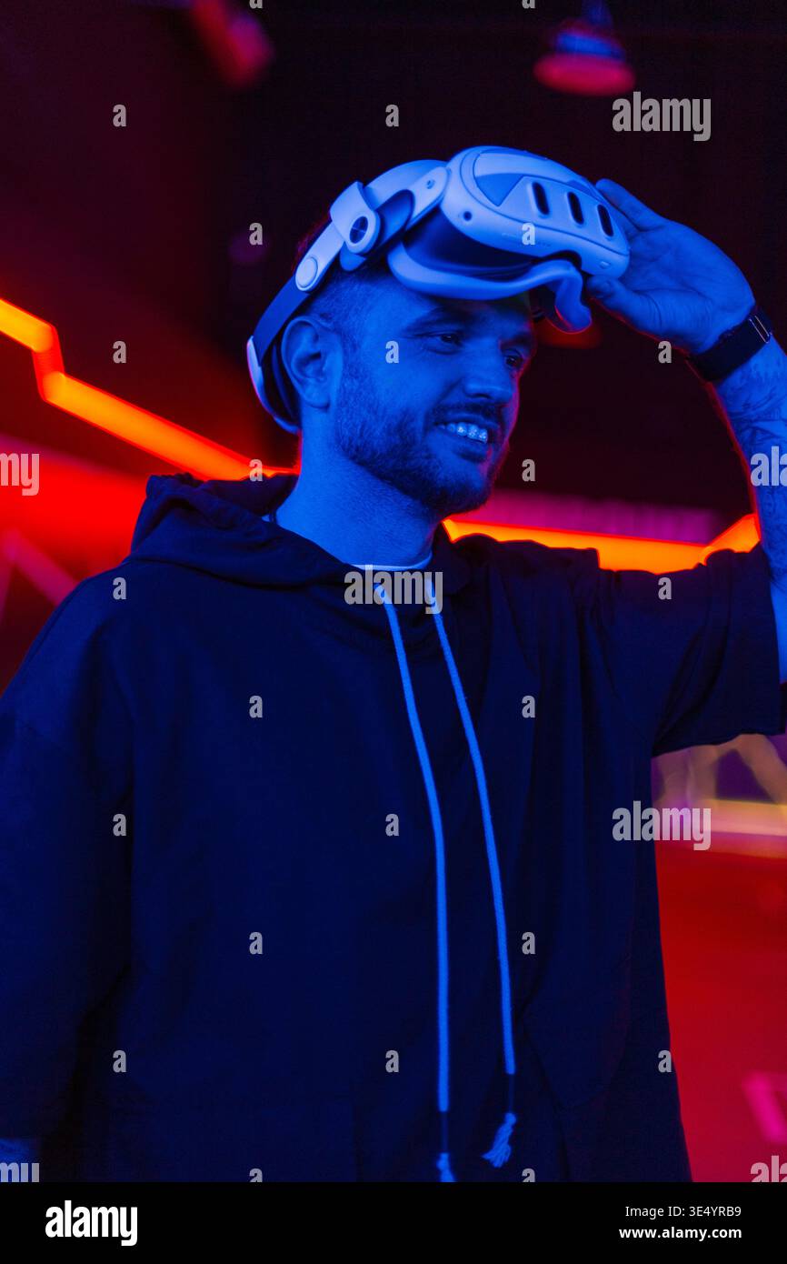 Cooler, gutaussehender Modetechniker, der eine VR-Brille in einem dunklen Raum mit Neonlicht trägt. Virtuelle Realität Stockfoto