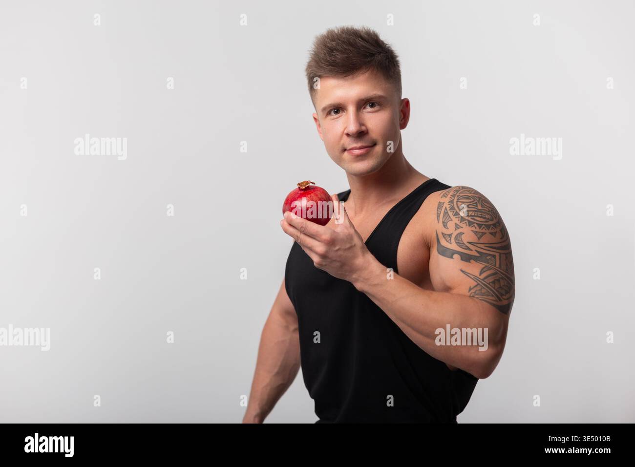 Gutaussehender muskulöser athletischer gesunder Mann, der Granatapfelfrucht hält und in die Kamera blickt. Granatapfelfrucht und Vitamine. Diät Stockfoto