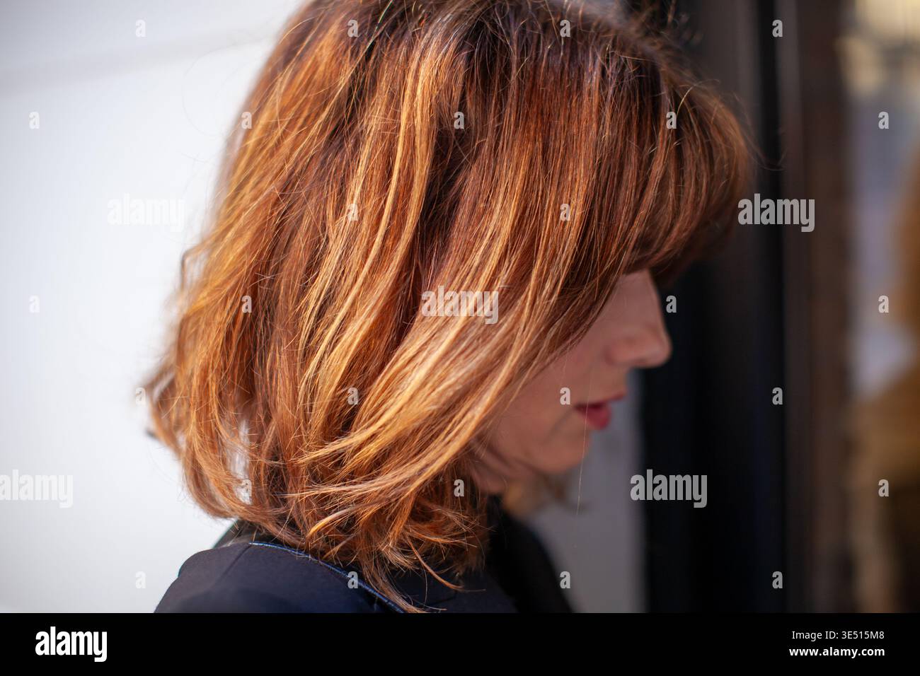 Frau mit schulterlangem braunem Haar und Highlights steht im Profil vor einem verschwommenen Hintergrund und zeigt eine moderne Frisur und natürliche Schönheit Stockfoto