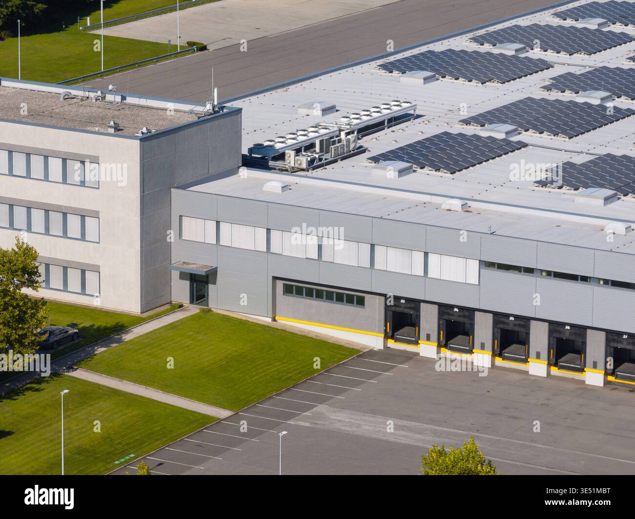 Drohne erfasst ein Logistikzentrum, in dem Lagerbetrieb und Lkw unter klarem Himmel in einem städtischen Gebiet dargestellt werden. Stockfoto