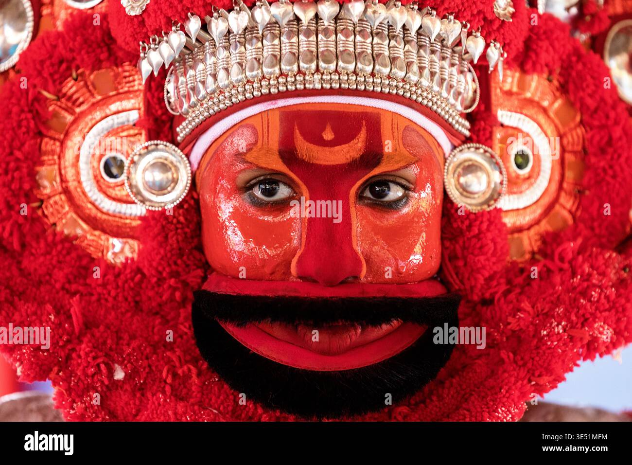 Nahaufnahme eines Theyyam-Künstlers mit raffinierten roten Kopfbedeckungen und traditioneller Gesichtsfarbe in einem Dorf in der Nähe von Kannur, Kerala, Indien Stockfoto