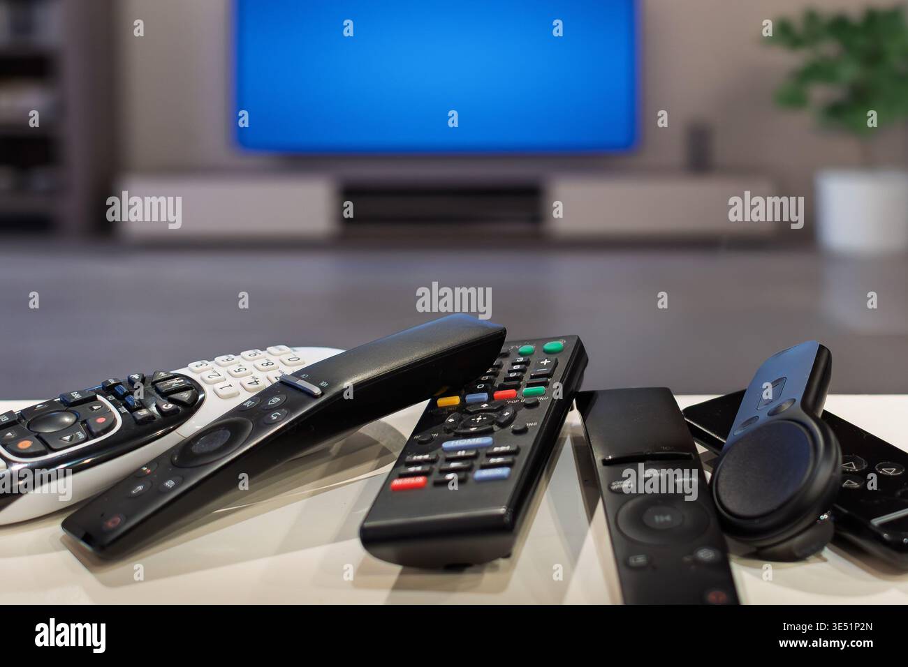 Eine Gruppe von generischen Fernbedienungen auf einem Tisch mit einem breitbildfernseher im Hintergrund eines Wohnzimmers. Stockfoto