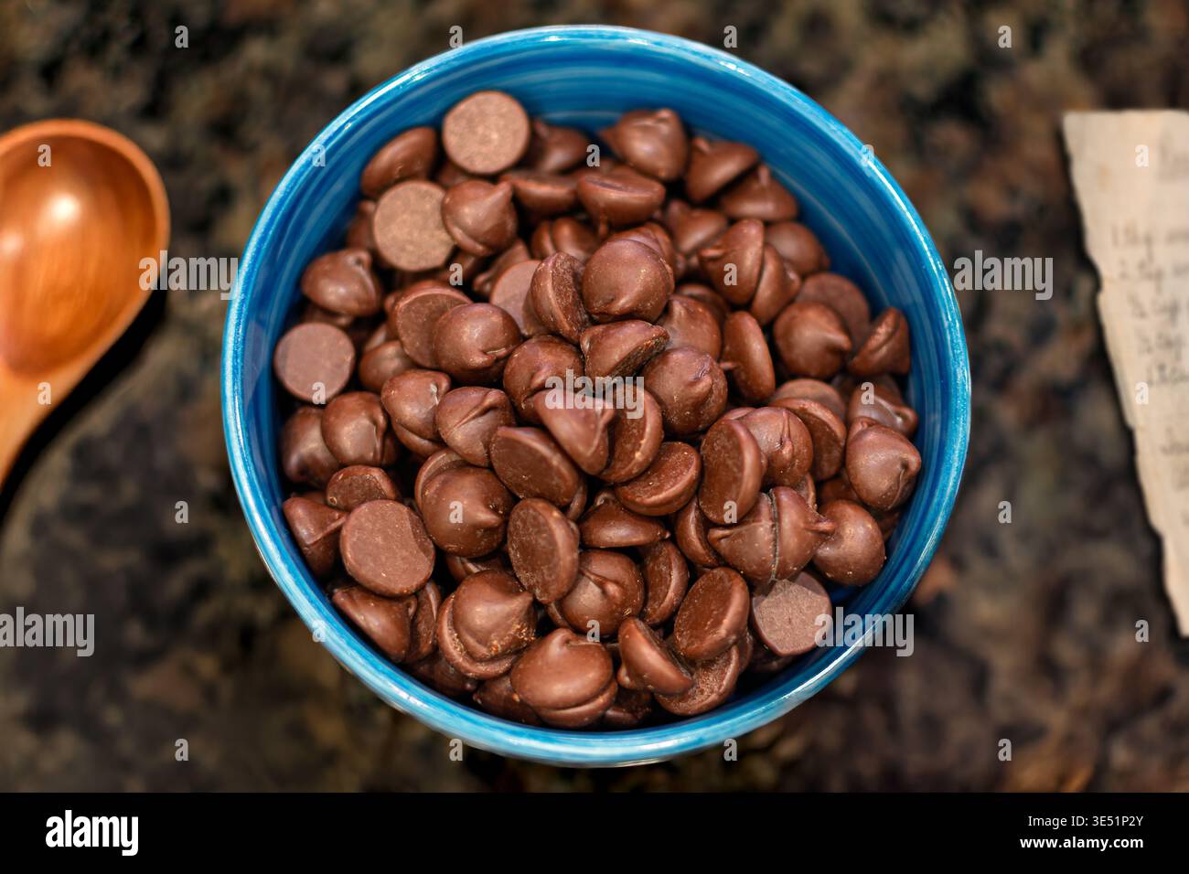 Eine kleine Schüssel mit Milchschokolade-Chips, dazu ein Holzlöffel und Rezept. Stockfoto
