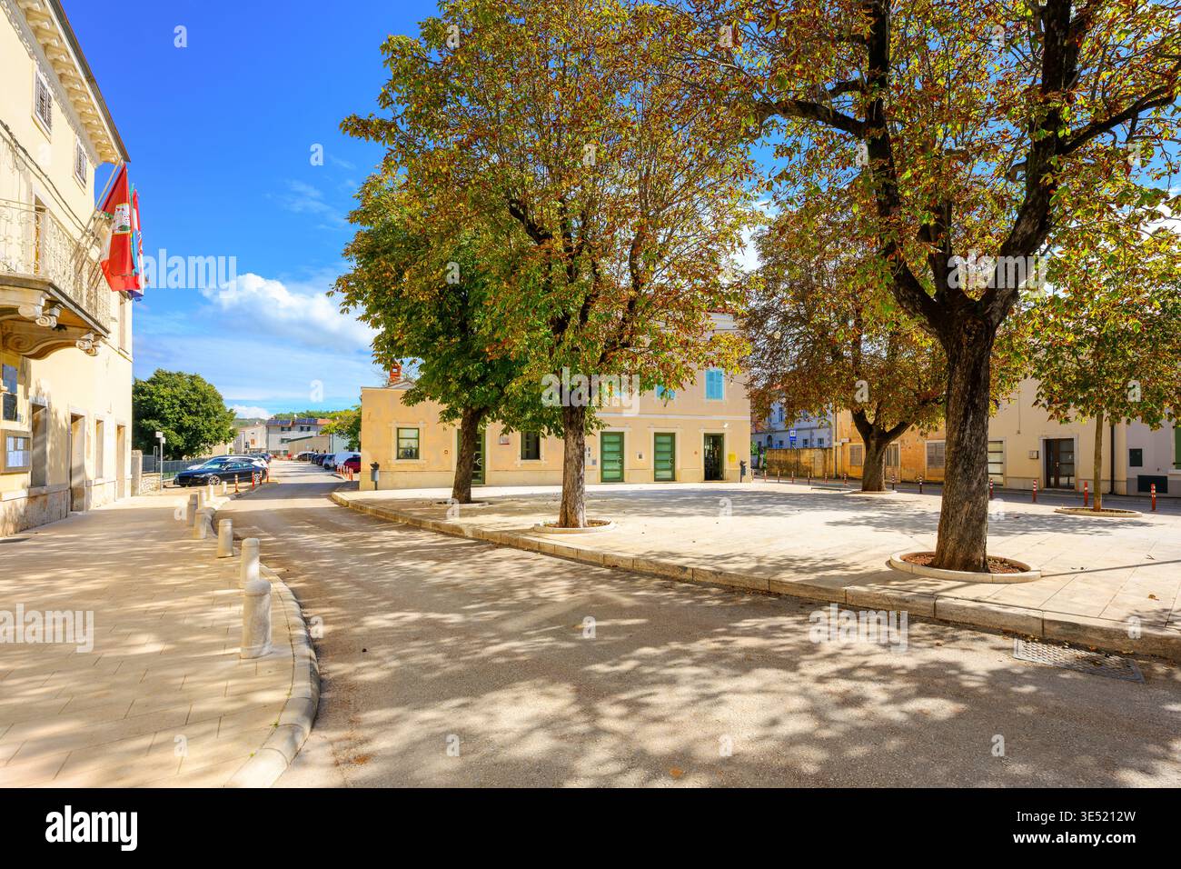 Ein von Bäumen gesäumter Platz gegenüber dem Rathaus in der ländlichen Bergstadt Višnjan, Kroatien. Stockfoto