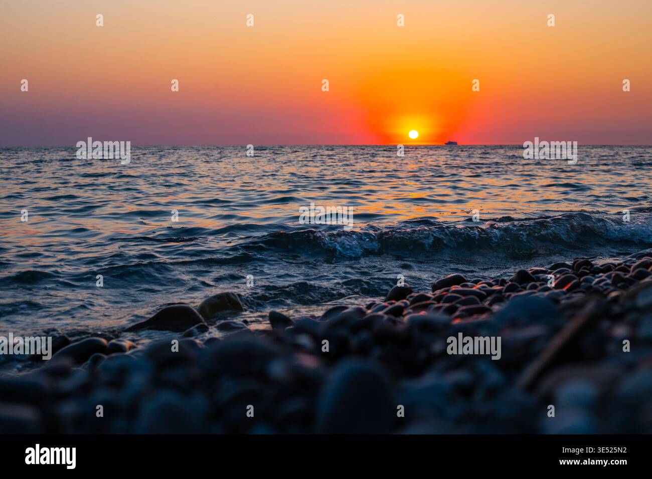 Ozeanwellen brechen an einem Kiesstrand unter einem leuchtend orangen Sonnenuntergang. Sonnenuntergang am Meer, Küstenwellen, Naturhintergrund Stockfoto