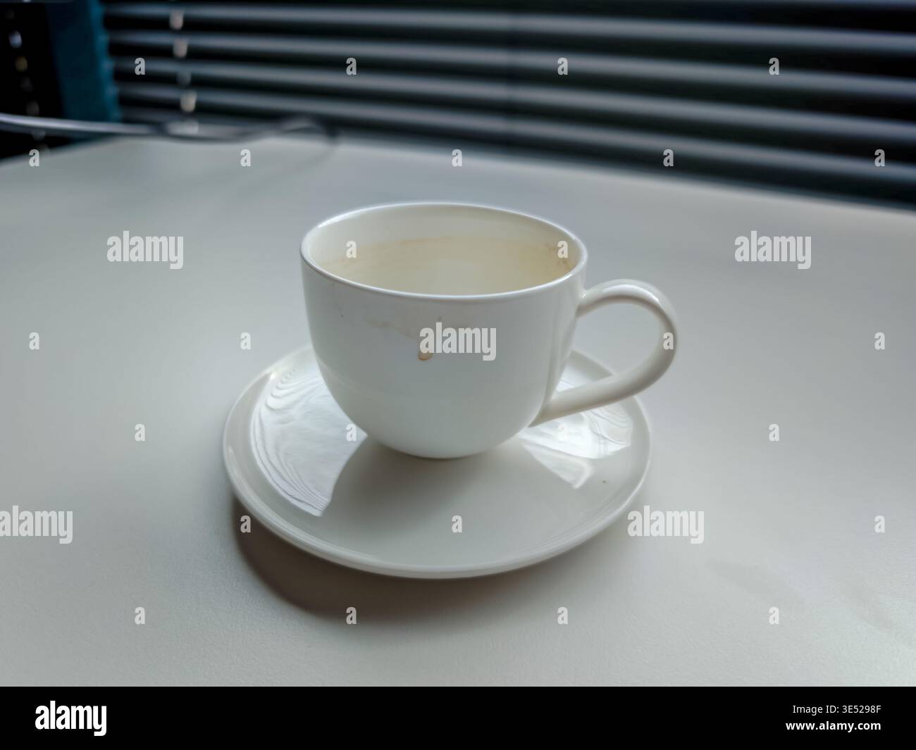 Schmutzige Kaffeetasse und Untertasse auf dem Schreibtisch, übrig gebliebene Kaffeeflecken, Unordnung am Arbeitsplatz, Büroalltag und zwanglose Schreibtischszene aus nächster Nähe Stockfoto