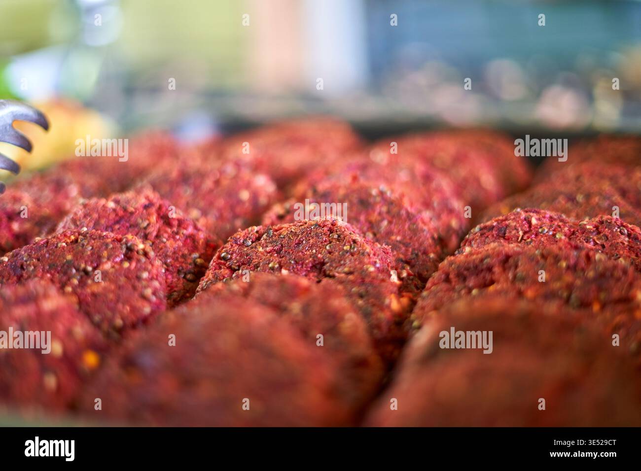 Nahaufnahme mehrerer roher Hamburger-Patties, die in ordentlichen Reihen angeordnet sind und ihre satte rote Farbe und sichtbare Würze von schwarzem Pfeffer und zeigen Stockfoto