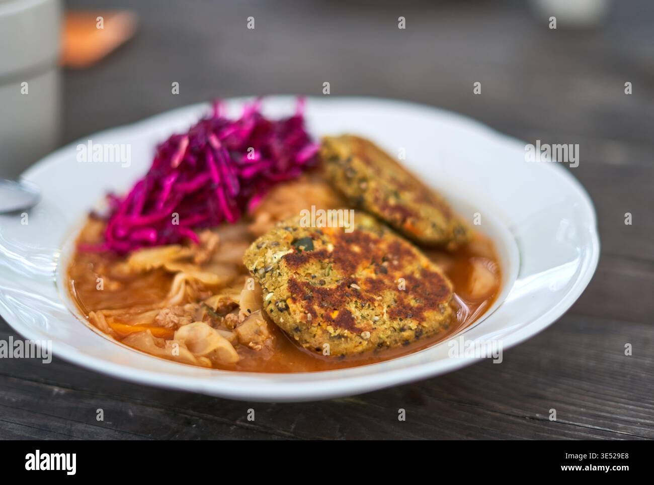 Ein Nahfoto einer weißen Keramikschale, gefüllt mit einer herzhaften Mahlzeit, auf einer dunklen hölzernen Tischoberfläche. Das Gericht enthält zwei goldbraune Stockfoto