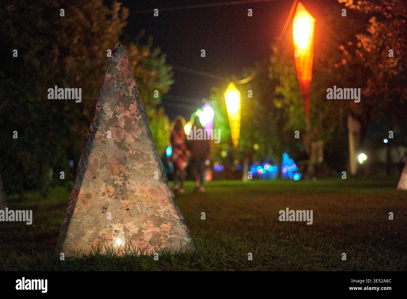 Nächtliche Outdoor-Szene mit einem verwitterten dreieckigen Stein- oder Betonmarker im Vordergrund auf grünem Gras, aufgenommen mit flachem Untergrund Stockfoto