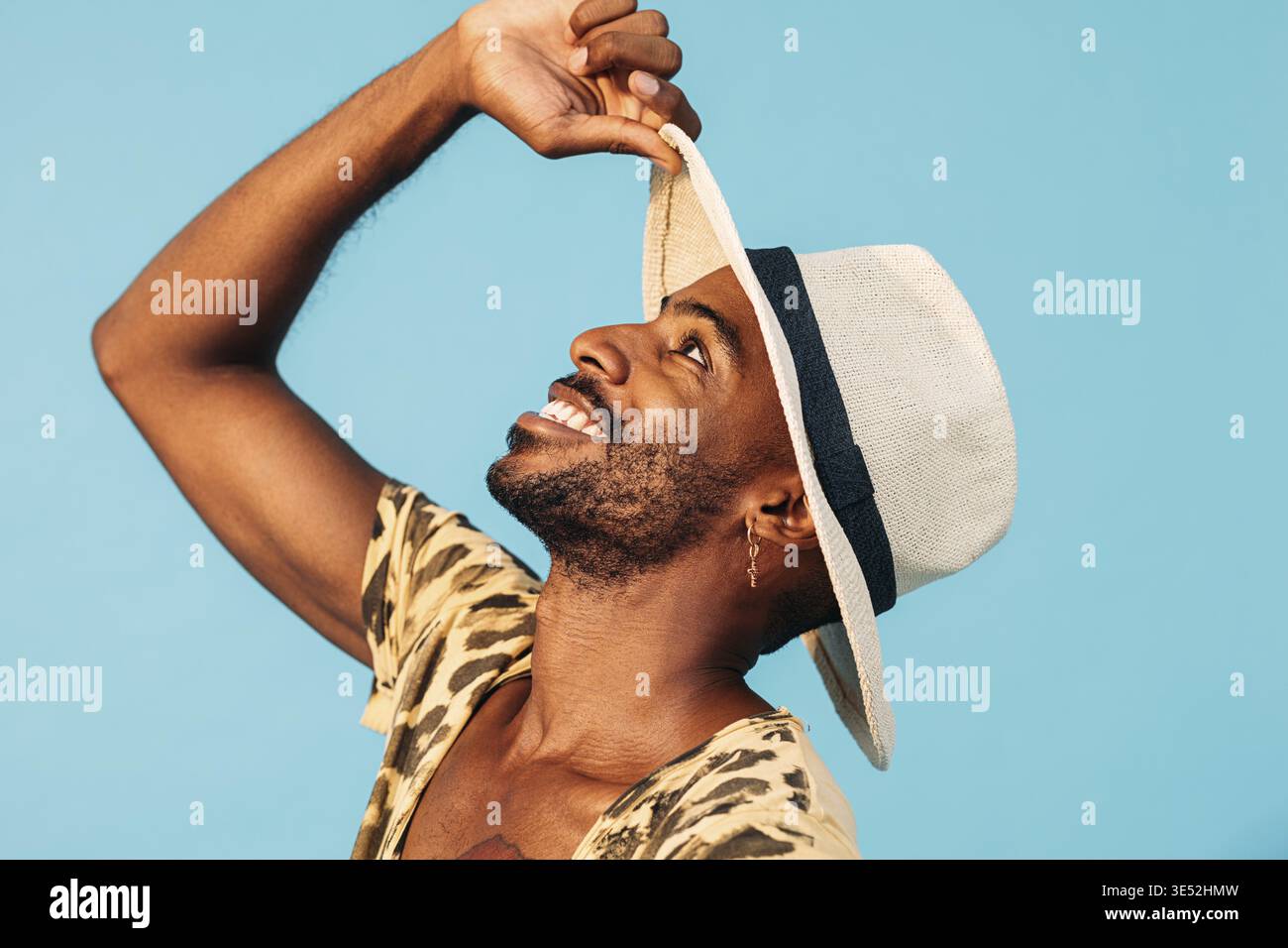 Glücklicher afroamerikanischer Mann mit Strohhut, der vor blauem Hintergrund aufschaut Stockfoto