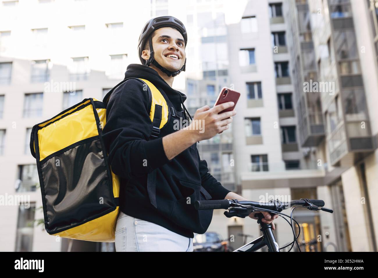 Porträt der Geburt Mann mit einem Mobiltelefon, trägt thermische Rucksack stehen gegen Wohngebäude Stockfoto