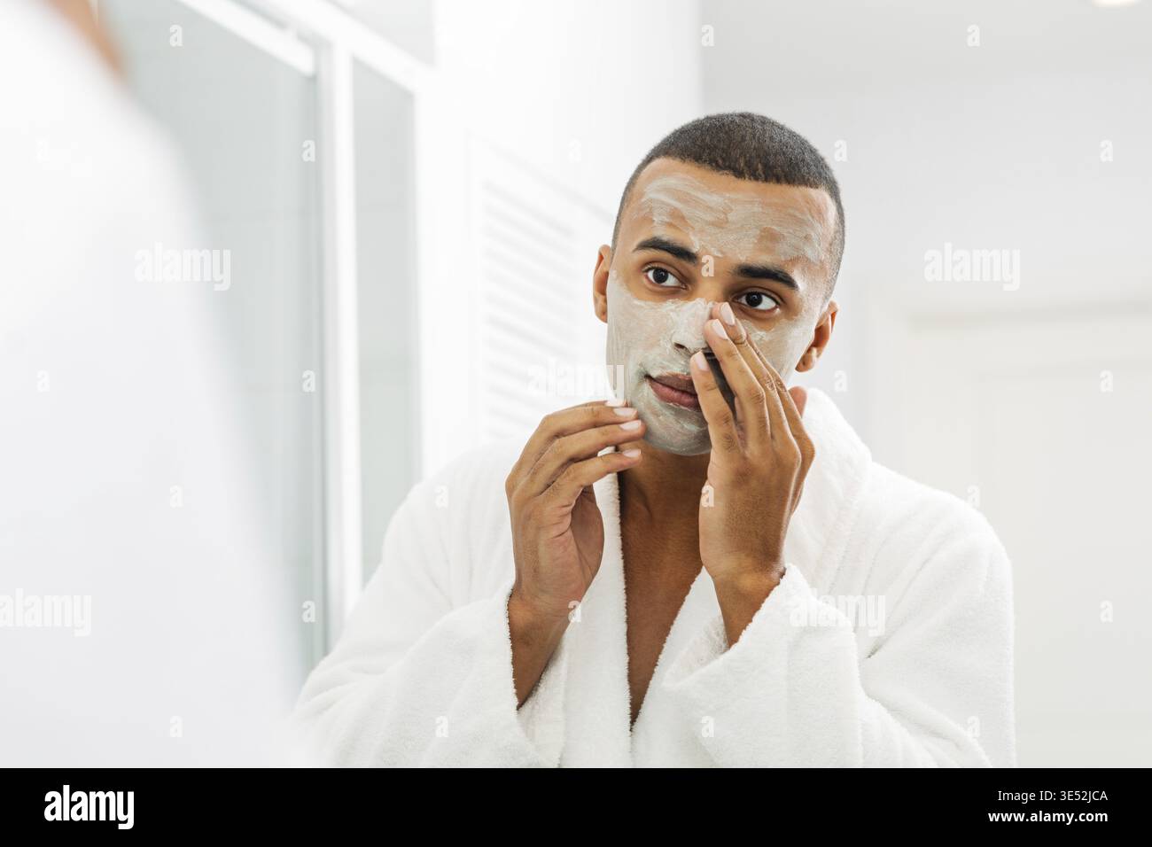 Junger Mann mit weißer Bademantel, die Gesichtsmaske im Badezimmer Stockfoto