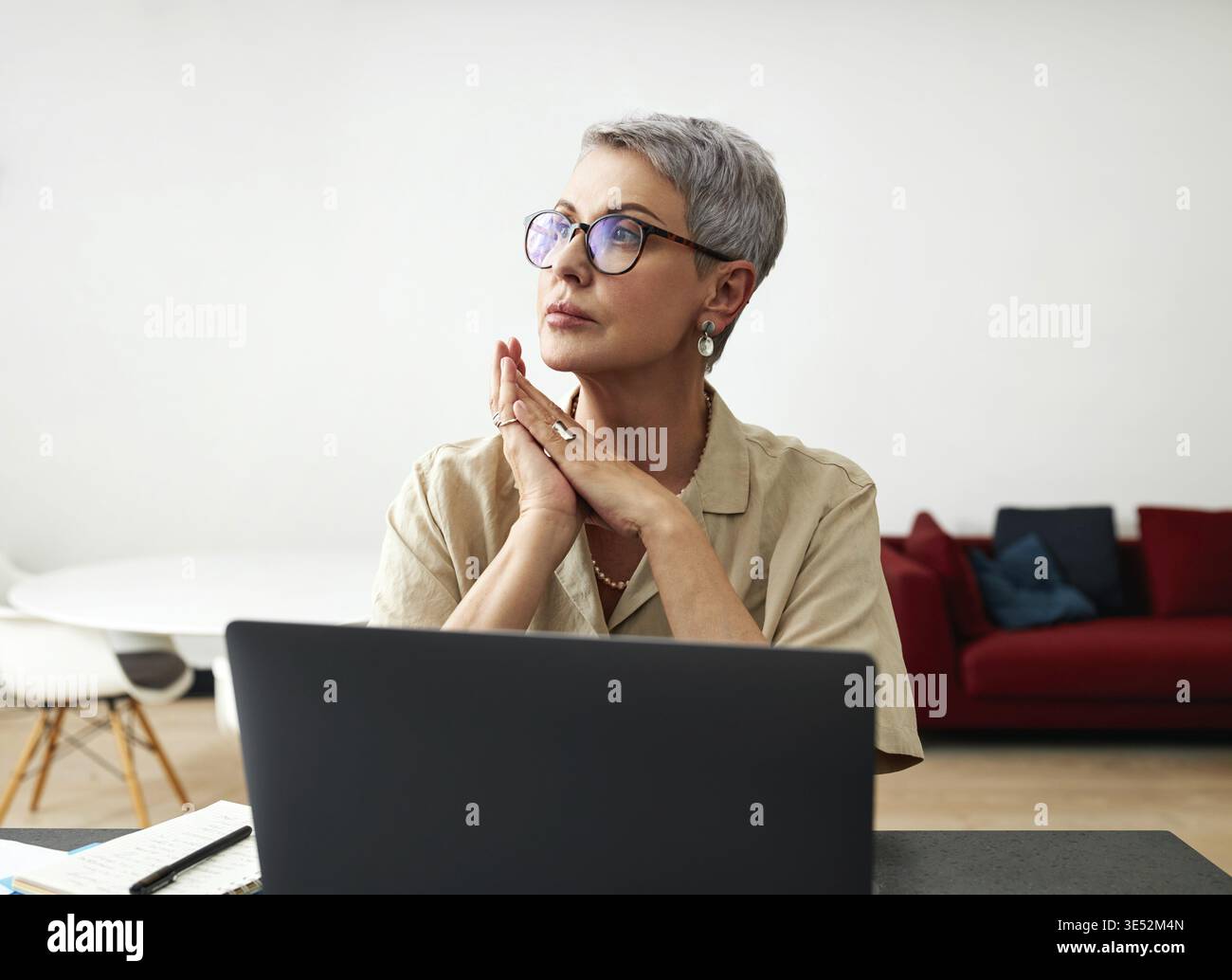 Stilvolle reife Frau in Brille am Schreibtisch sitzen Stockfoto