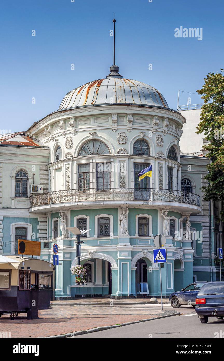 Ein wunderschönes historisches Gebäude mit einzigartigem architektonischen Stil und einer ukrainischen Flagge, die an einem sonnigen Tag unter einem hellblauen Himmel zu sehen ist Stockfoto