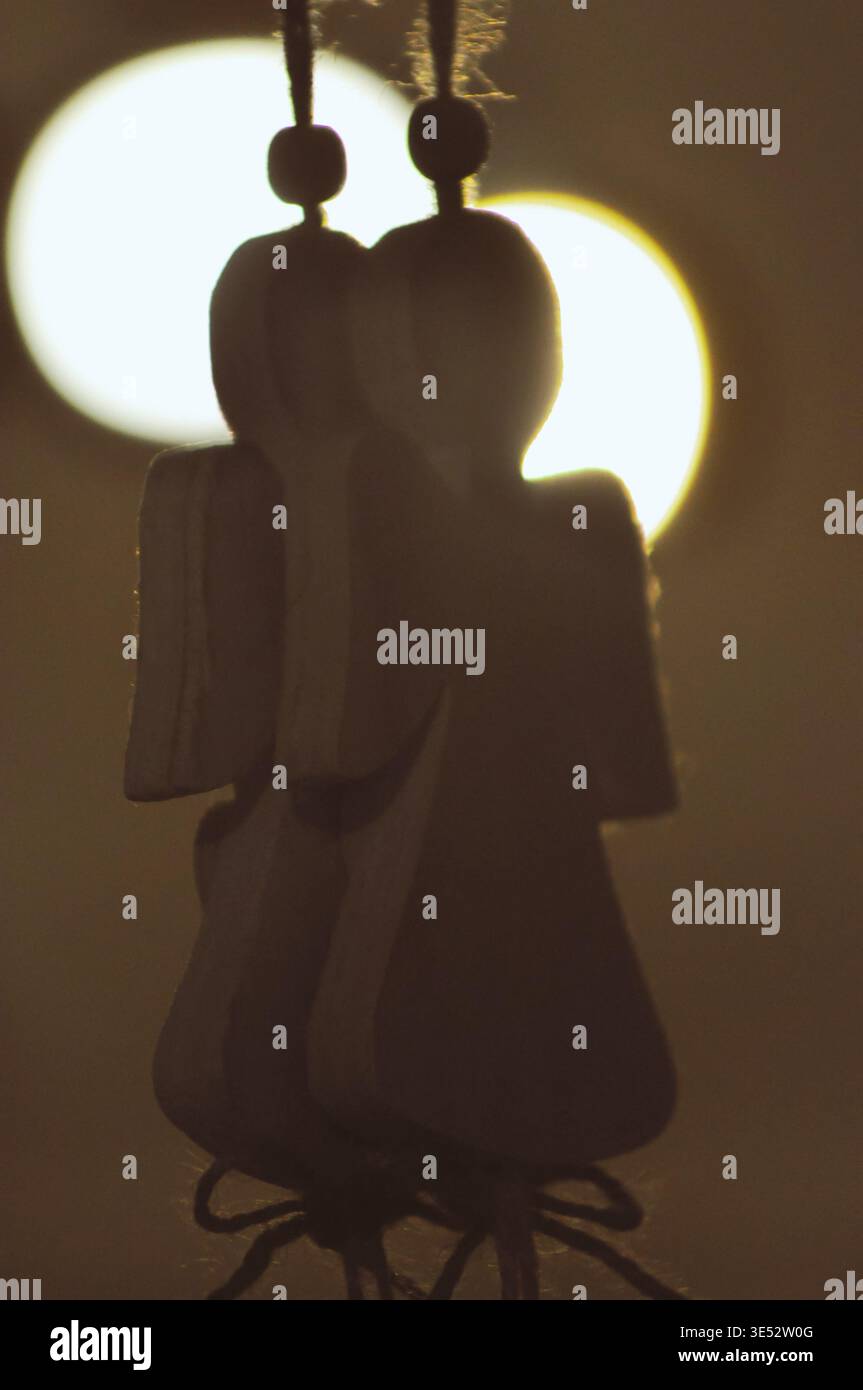 Figuren von Weihnachtsengeln aus Holz an einem Seil. Silhouette auf dem Hintergrund glühender Kugeln Stockfoto