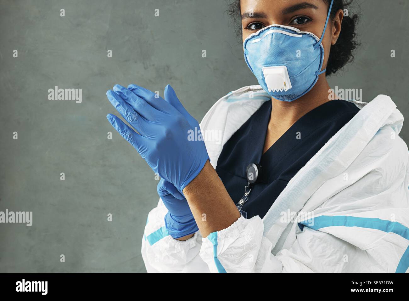 Junge medizinische Mitarbeiterin zieht chirurgische Handschuhe an und schaut auf die Kamera Stockfoto