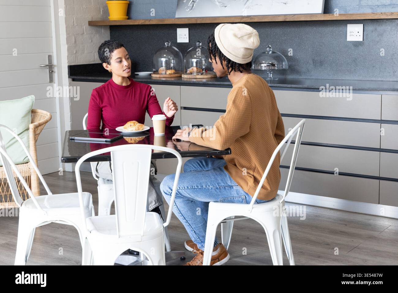 Afroamerikanische Freunde unterhalten sich am Glastisch mit Croissant und Telefon im Café Stockfoto