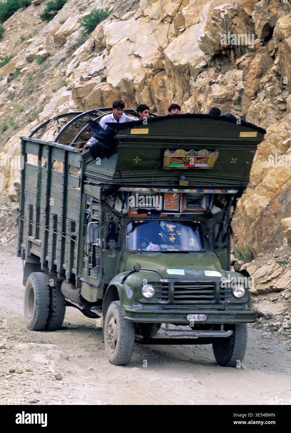 Ein Lkw fährt auf einer unebenen Straße in Pakistan mit mehreren Fahrgästen oben. Die Szene zeigt das tägliche Leben und Reisen in der Region. Stockfoto