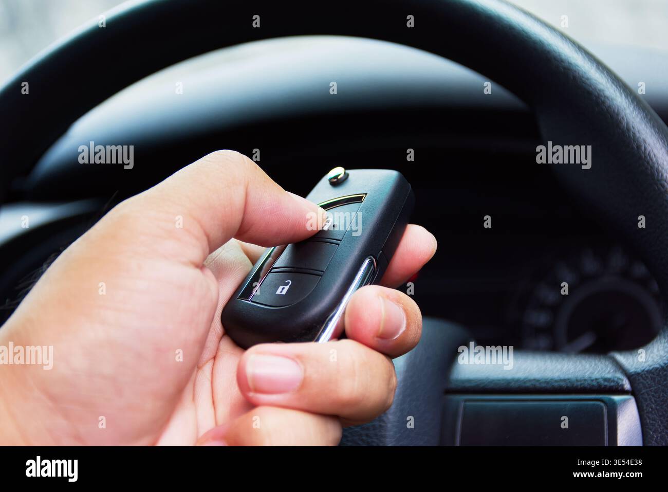 Ferngesteuerte Autoschlüssel-Fernbedienung: Eine Hand hält einen modernen schwarzen Autoschlüssel und drückt die Verriegelungstaste in der Fahrerkabine, während sich das Lenkrad im befindet Stockfoto