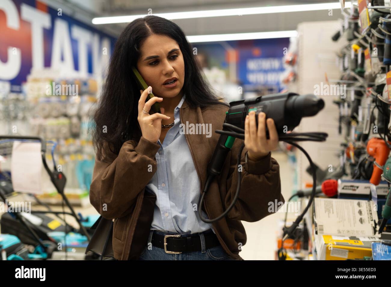 Frau, die eine Übung hält, während sie in einem Eisenwarengeschäft telefoniert Stockfoto