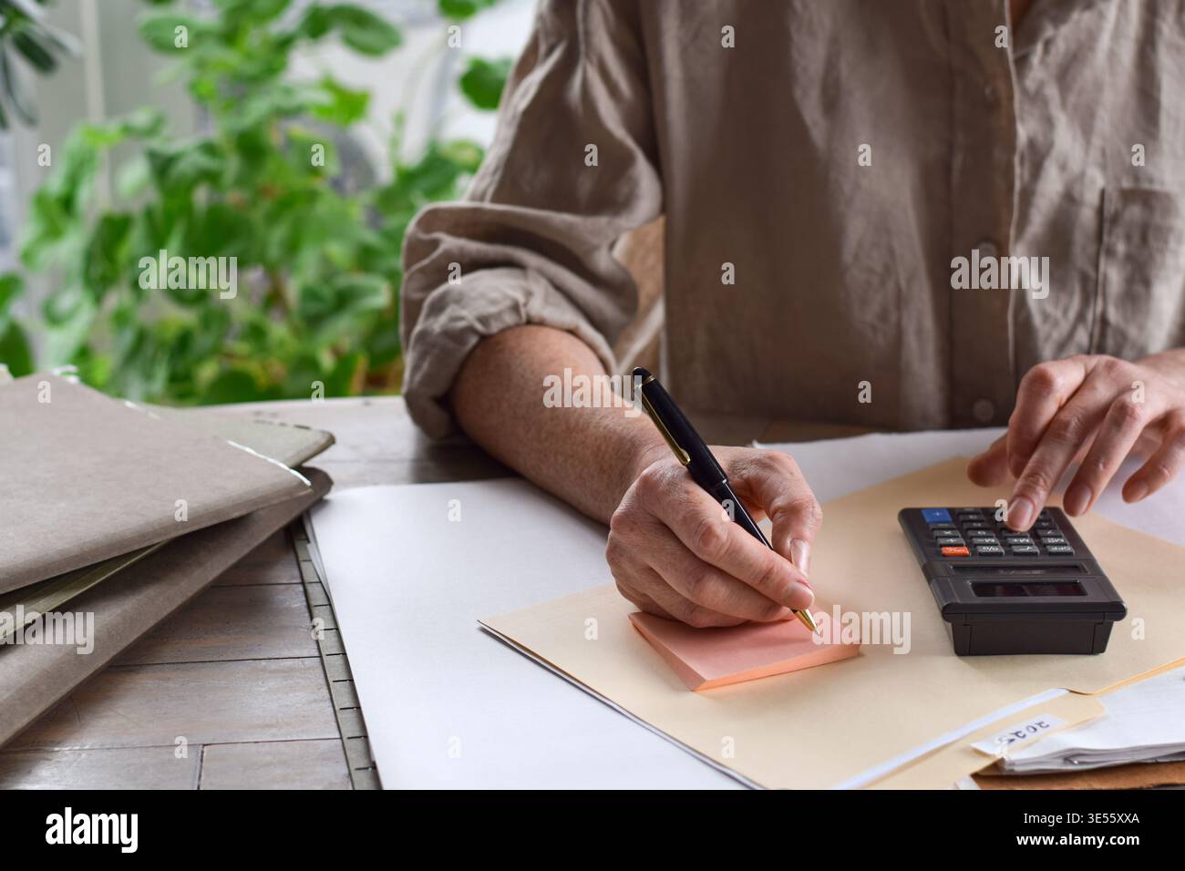 Frau, die auf Haftnotizen schreibt, während sie am Schreibtisch einen Rechner mit 2025 Steuerordner benutzt. Home-Office-Szene konzentriert sich auf Finanzplanung, Bud Stockfoto