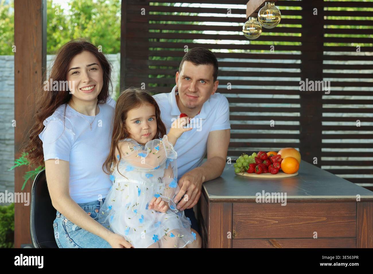 Glückliche Familie mit Kind, das draußen am Holztisch sitzt Stockfoto