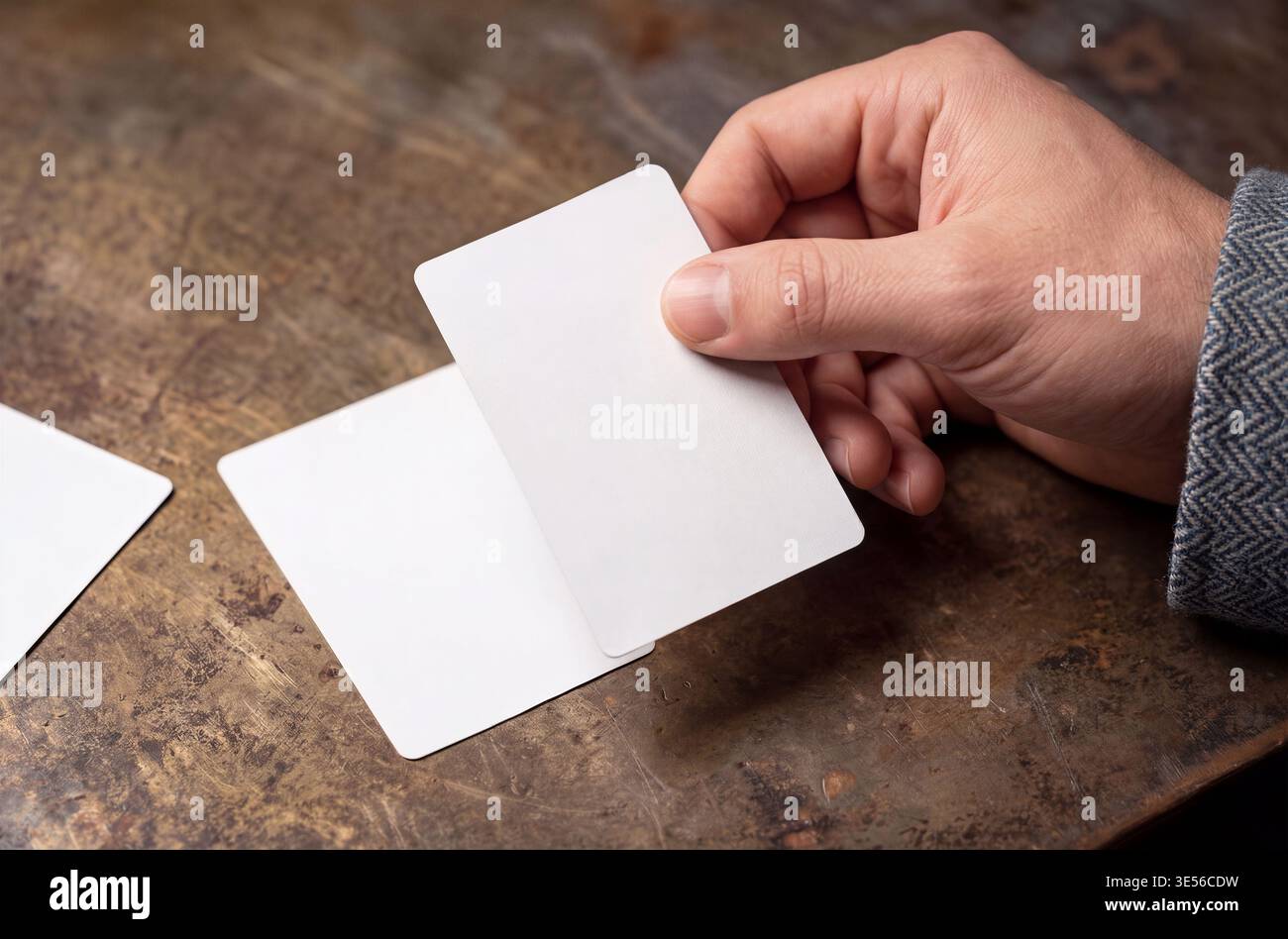 Mockup einer Hand, die eine leere weiße Karte über einem rustikalen Holztisch hält, mit anderen Karten. Stockfoto