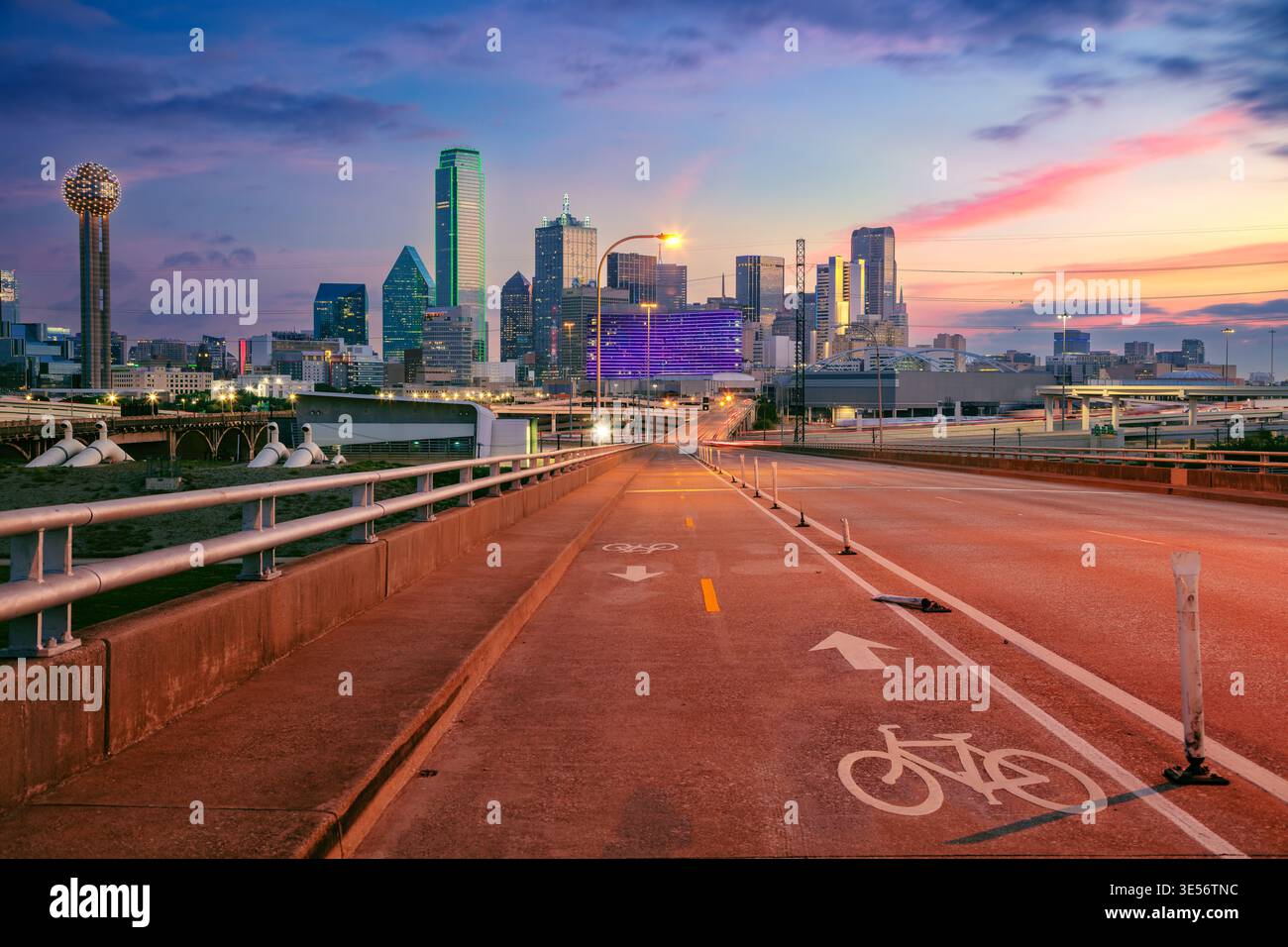 Das Stadtzentrum von Dallas, Texas, USA, wird während des Sonnenaufgangs dargestellt. Die Skyline verfügt über moderne Wolkenkratzer. Eine Autobahn und ein Radweg führen in die Stadt, ganz oben Stockfoto