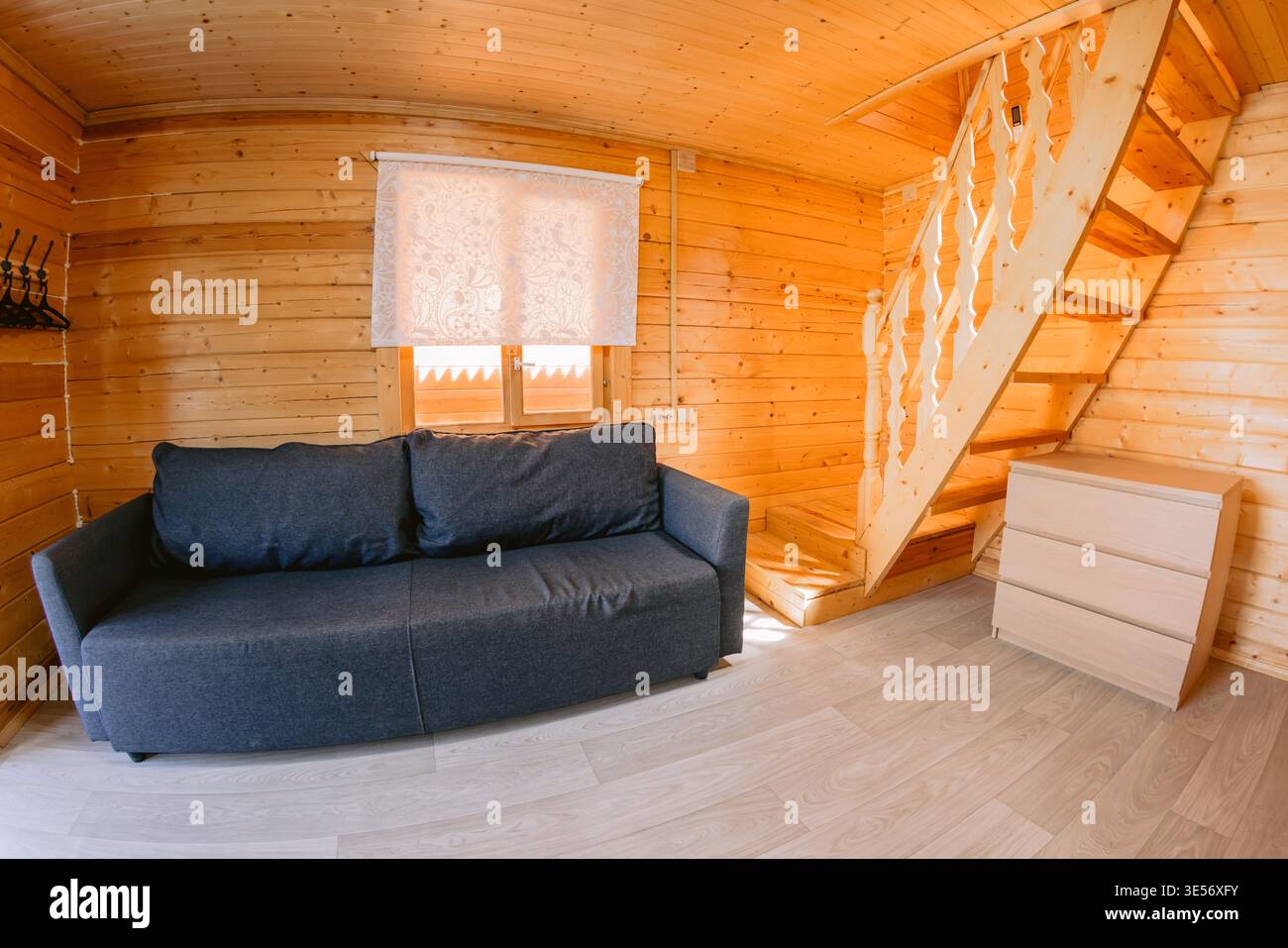 Gemütliches hölzernes Wohnzimmer mit Sofa, Treppe und warmer natürlicher Inneneinrichtung im Kabinenstil, Gastfamilie Stockfoto