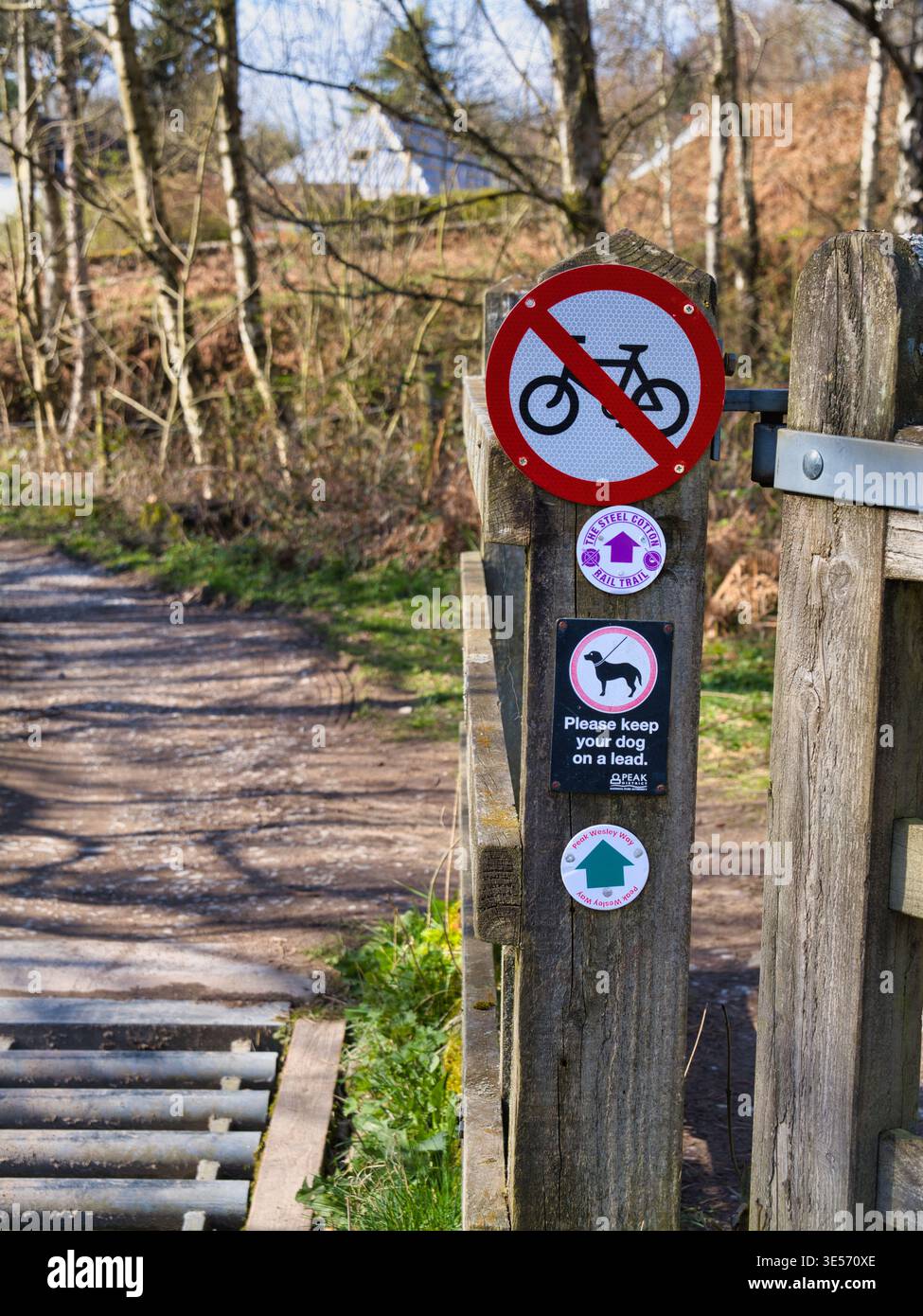 Derbyshire, UK - 26. März 2026: Holzpfosten am Wanderweg mit Schildern „Kein Radfahren“ und „Hund an der Leine“ neben einem Feldweg in Derbyshire, UK, helles Frühlingslicht und klare Details im Freien Stockfoto