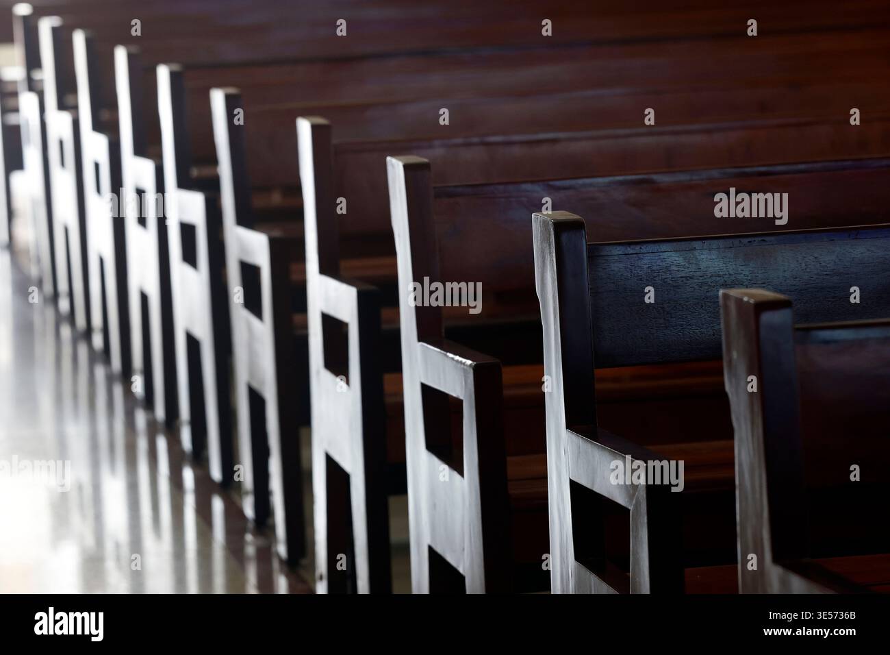 Leere polierte Holzbänke säumen das Kirchenschiff einer vietnamesischen katholischen Kirche in geometrischer Symmetrie. Ho-Chi-Minh-Stadt. Vietnam. Stockfoto