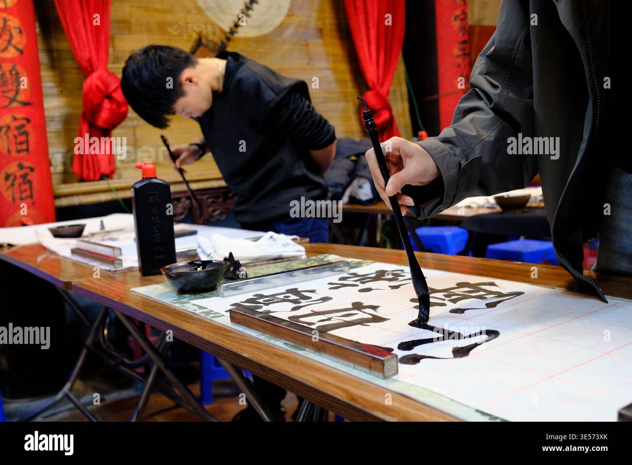 Kalligraphie-Workshop-Szene mit zwei Teilnehmern, die mit Tintenbürsten auf Reispapier schreiben. Hanoi. Vietnam. Stockfoto