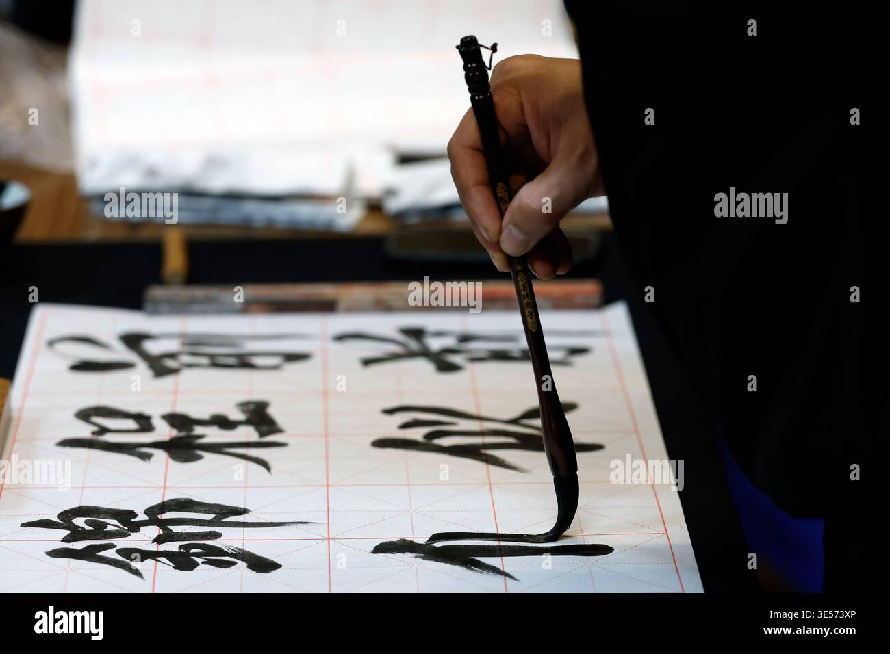 Nahaufnahme einer Hand, die einen Kalligraphiebürsten hält, die kräftige chinesische Schriftzeichen auf gerastertes Papier schreibt. Hanoi. Vietnam. Stockfoto