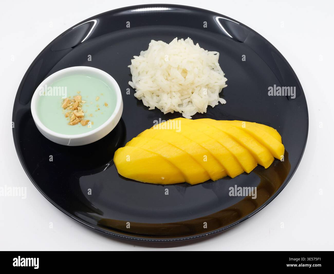 Asiatische Küche. Klassisches thailändisches Mango-Reisdessert mit Kokosnusscreme-Sauce auf schwarzem Teller. Stockfoto